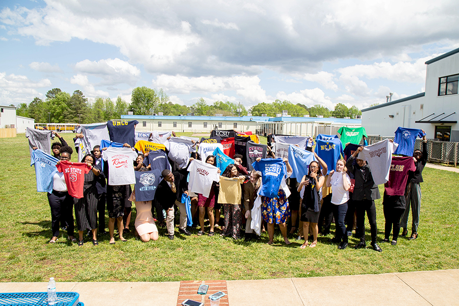 <p>Students at KIPP Gaston hold up T-shirts of colleges they were admitted to on College Signing Day. (Richard Whitmire/The 74)</p>
